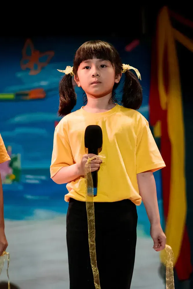 A little girl in a yellow shirt is holding a microphone.