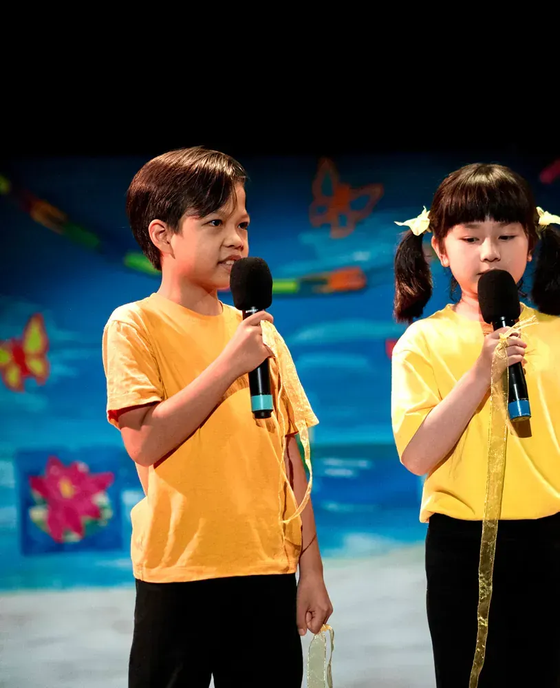A boy and a girl singing into microphones on a stage