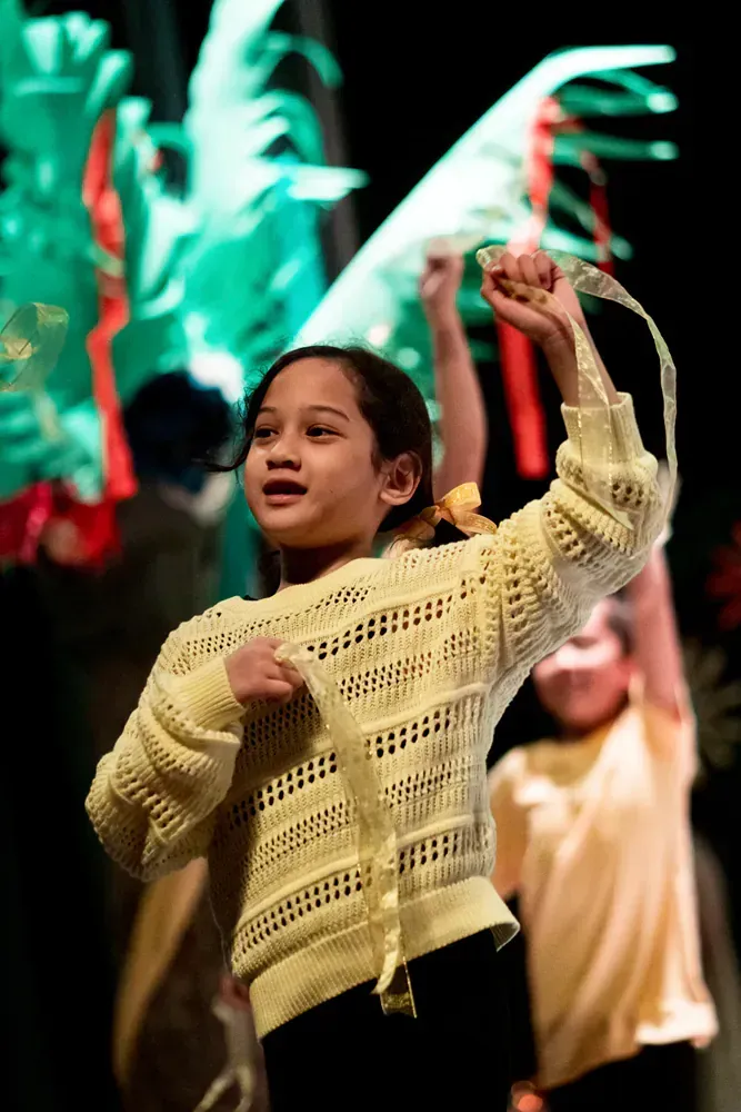 A young girl in a yellow sweater is dancing on a stage.