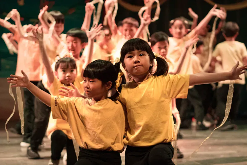 A group of children in yellow shirts are dancing on a stage.