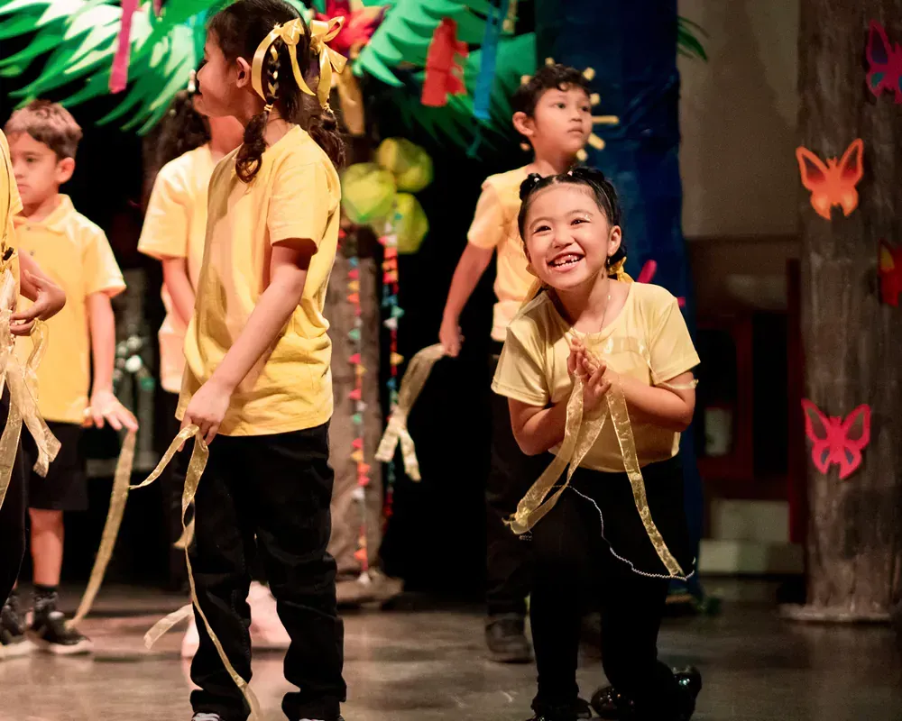 A group of children in yellow shirts are dancing on a stage
