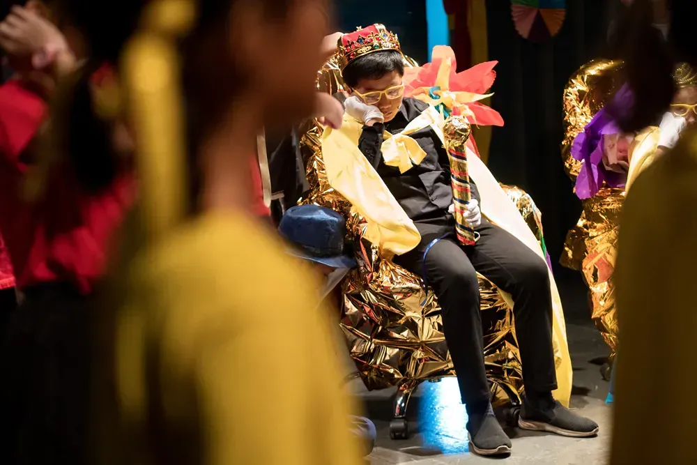 A man in a costume is sitting on a chair in a crowd of people.