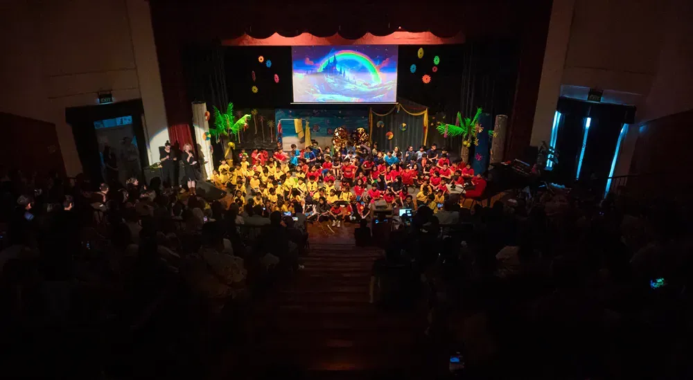 A large group of people are sitting in a dark auditorium watching a concert.