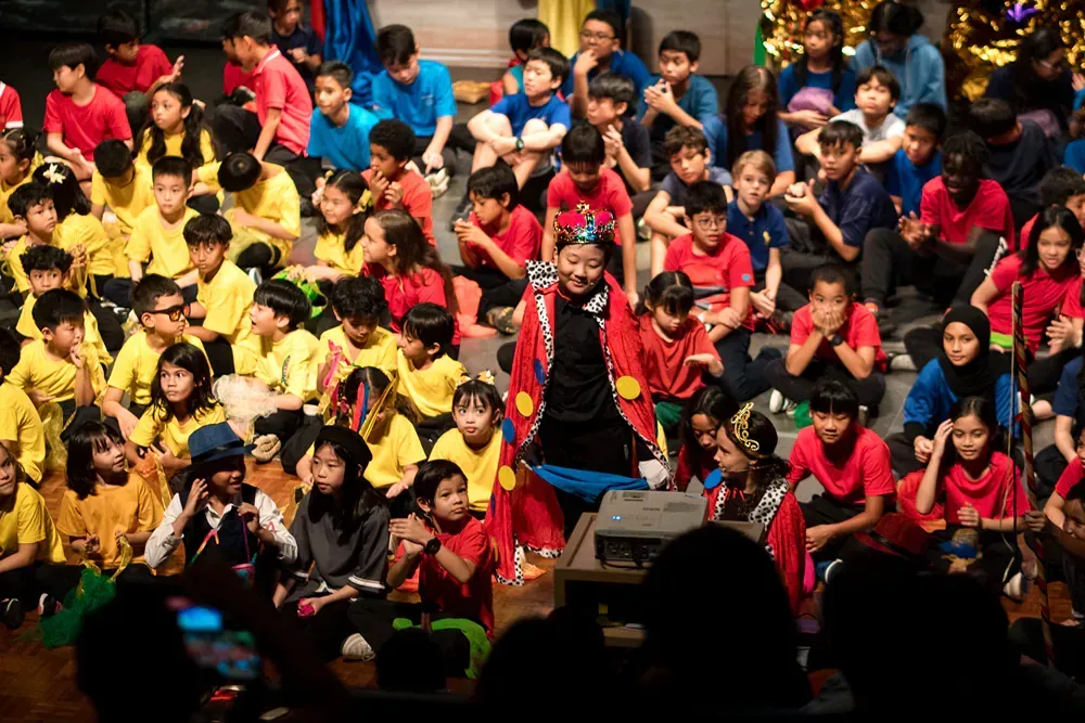 A large group of children are sitting on the floor in front of a stage.