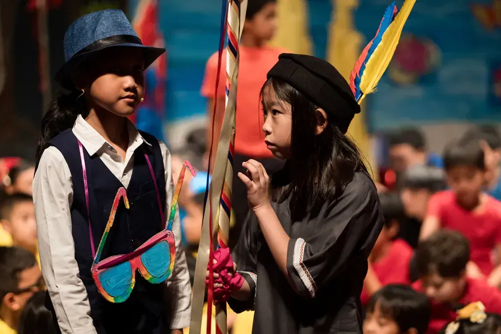 Two young girls dressed in costumes are standing next to each other in front of a crowd.