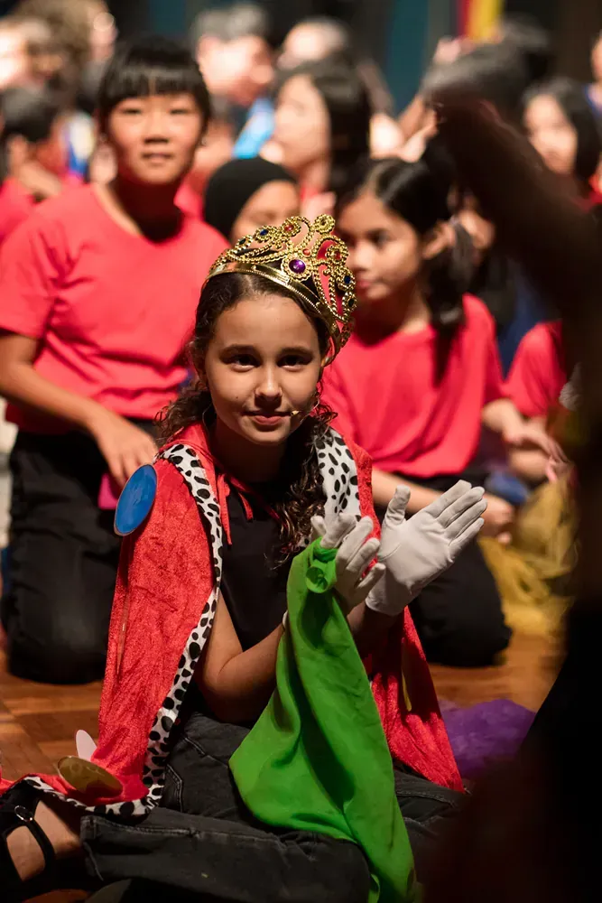 A young girl is wearing a crown and gloves while sitting on the floor.
