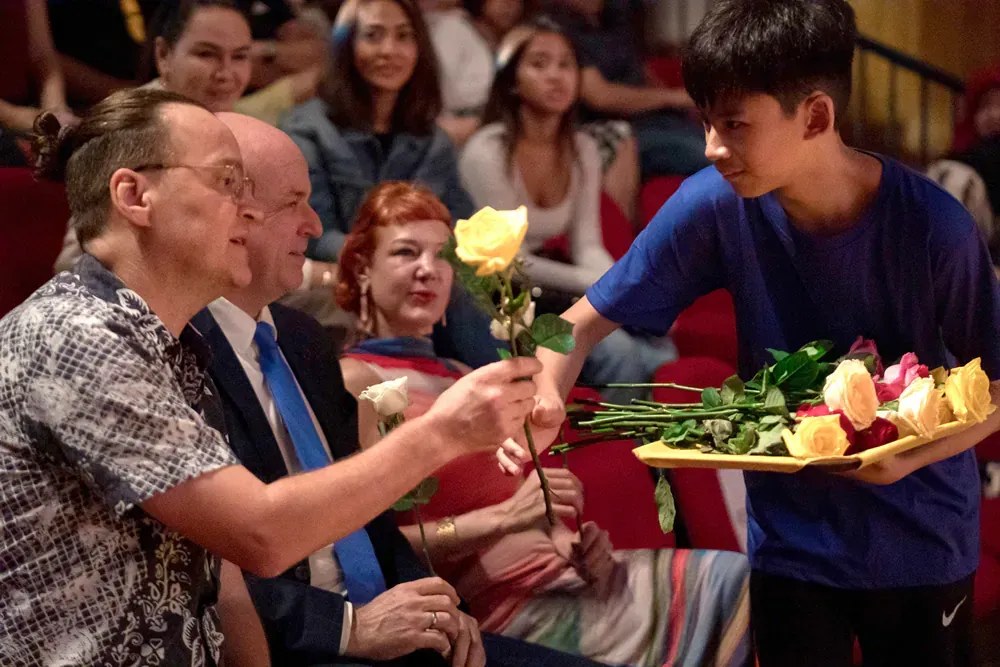 A boy is holding a tray of flowers in front of a group of people.
