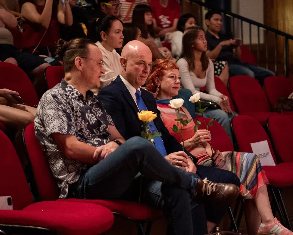 A group of people are sitting in red chairs holding flowers.