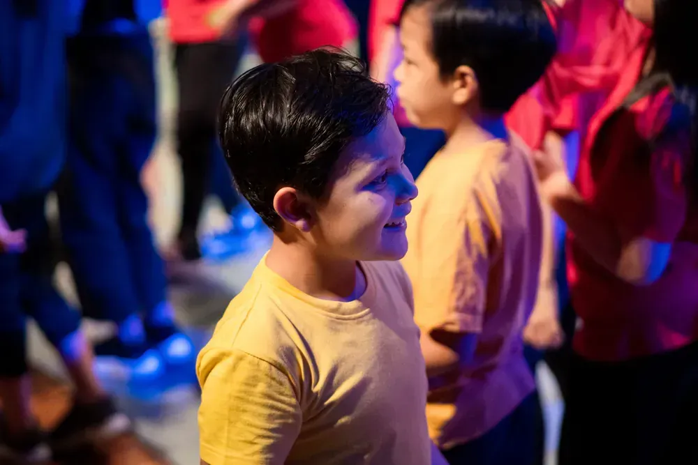A boy in a yellow shirt is standing in a crowd of people.