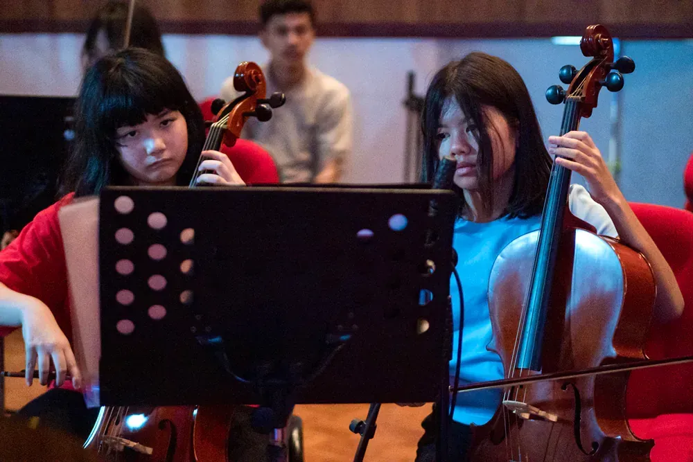 Two young girls are playing cello in an orchestra.