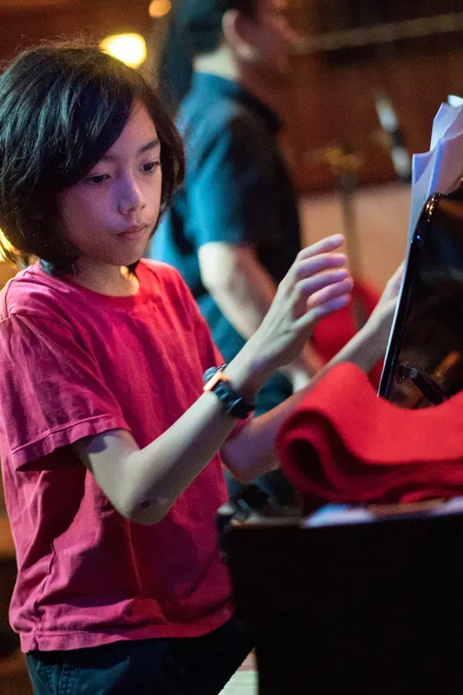 A young boy in a red shirt is playing a piano.