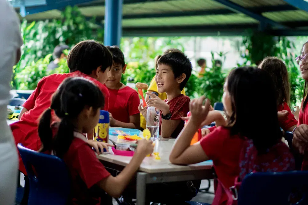 A group of children are sitting at a table eating food.