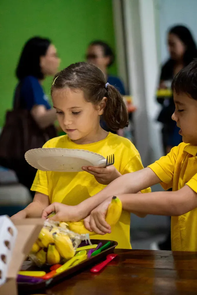 A boy and a girl are sitting at a table eating bananas.