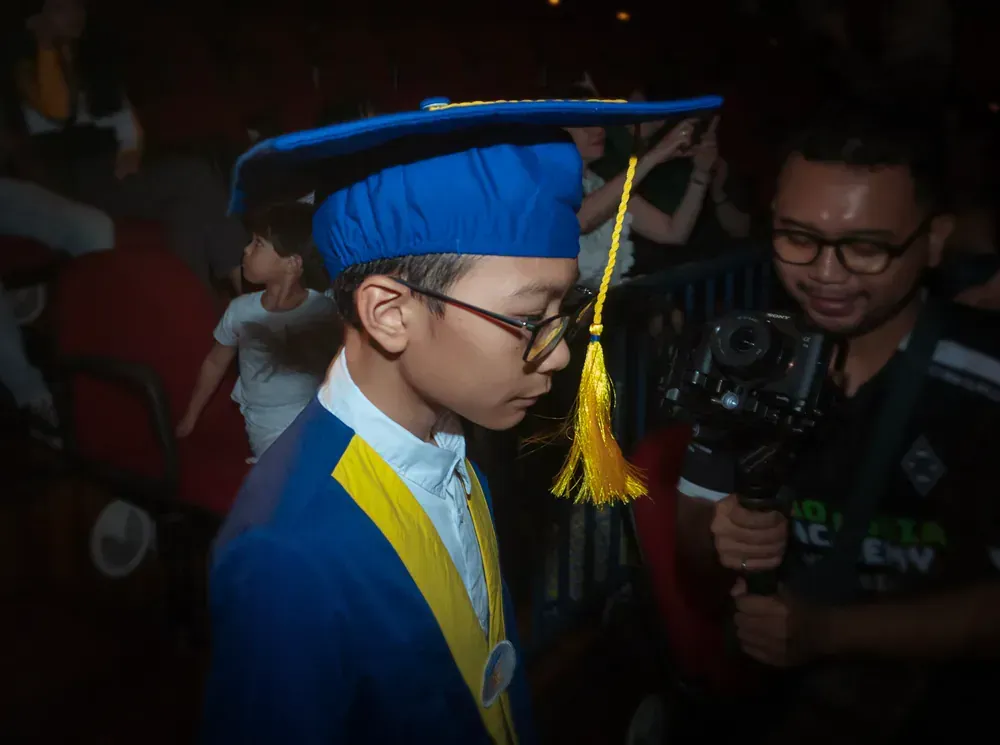 A young boy in a graduation cap and gown is standing in front of a camera.