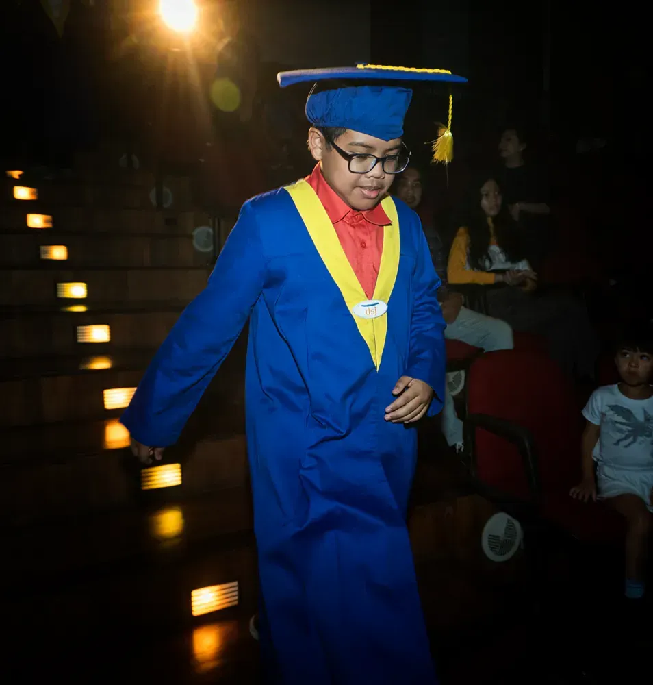 A young boy in a graduation cap and gown is walking down stairs.