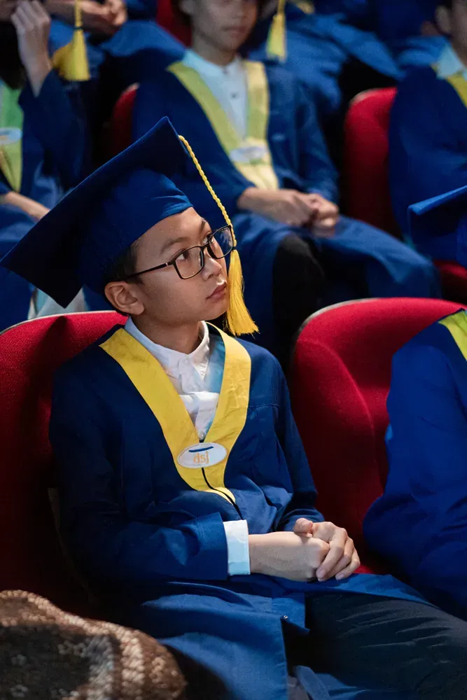 A boy in a graduation cap and gown is sitting in a theater.