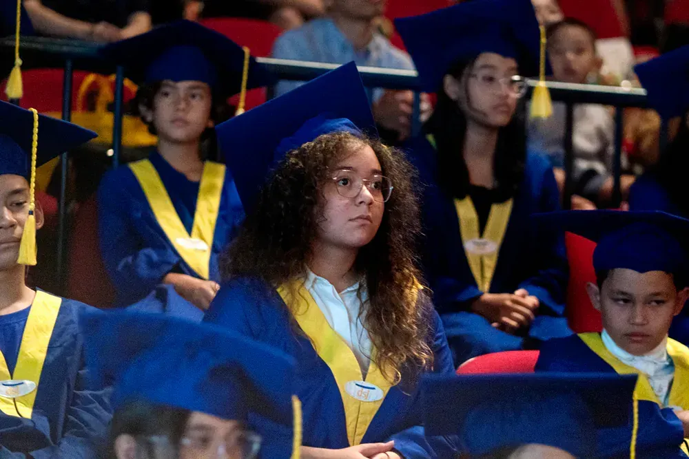 A group of children in graduation caps and gowns are sitting in a stadium.