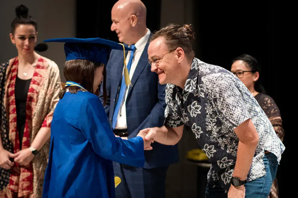 A man is shaking hands with a woman in a graduation cap and gown.