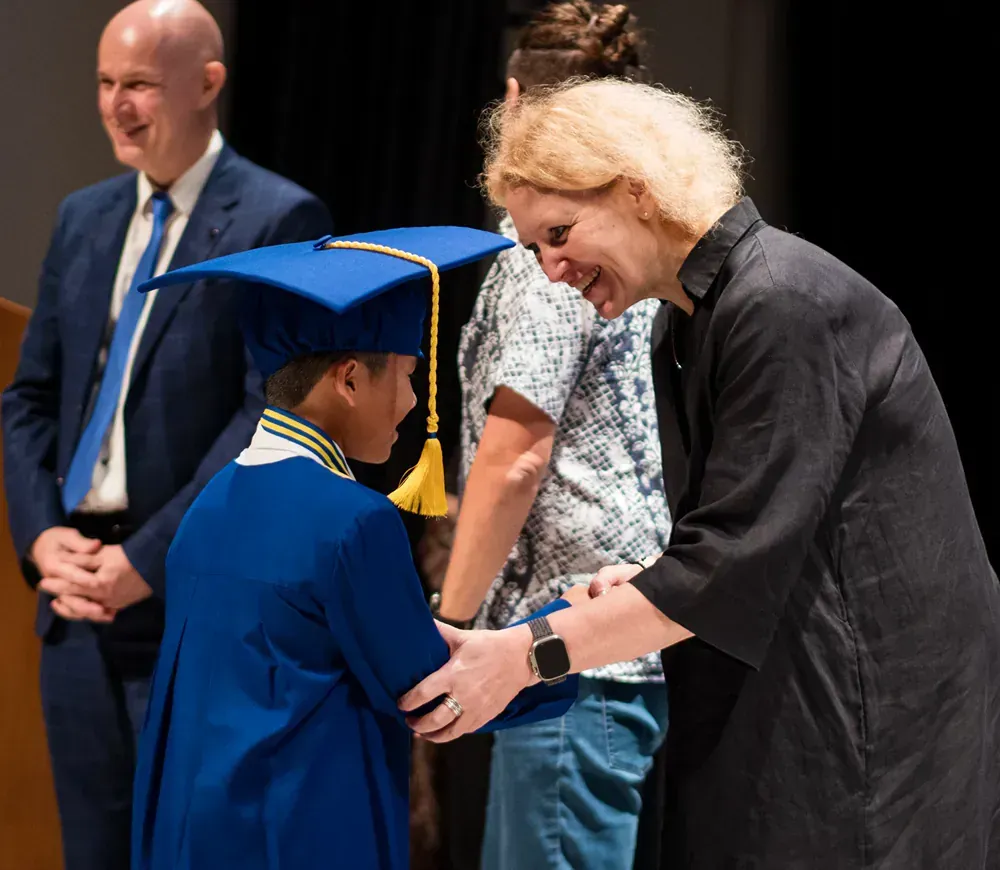 A girl in a graduation cap and gown is shaking hands with a woman