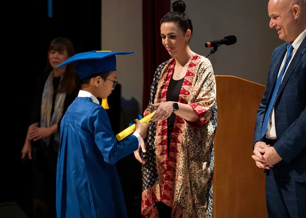 A woman is giving a diploma to a young boy in a graduation cap and gown.