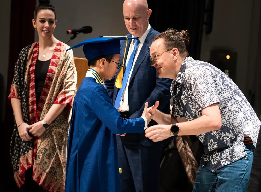 A boy in a graduation cap and gown is shaking hands with a man in a suit.