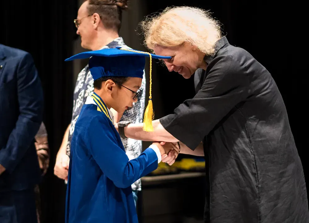 A woman is helping a young boy with his graduation cap and gown.