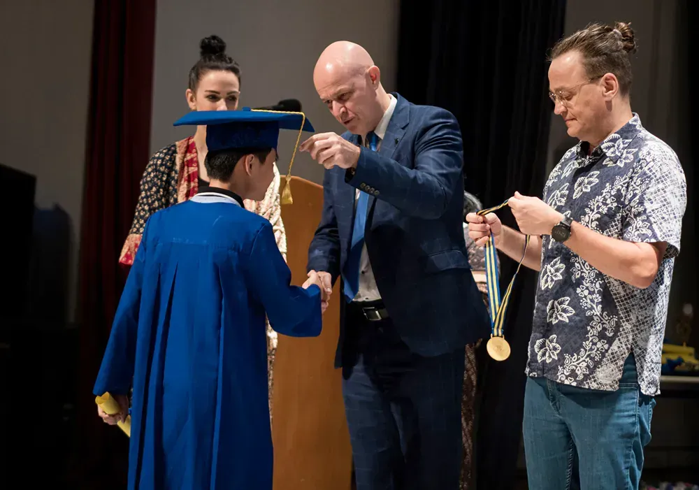 A man in a suit is giving a medal to a graduate.