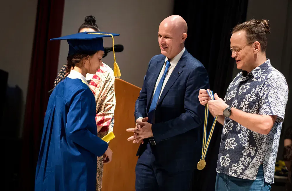A woman in a graduation cap and gown is being presented with a medal by two men.