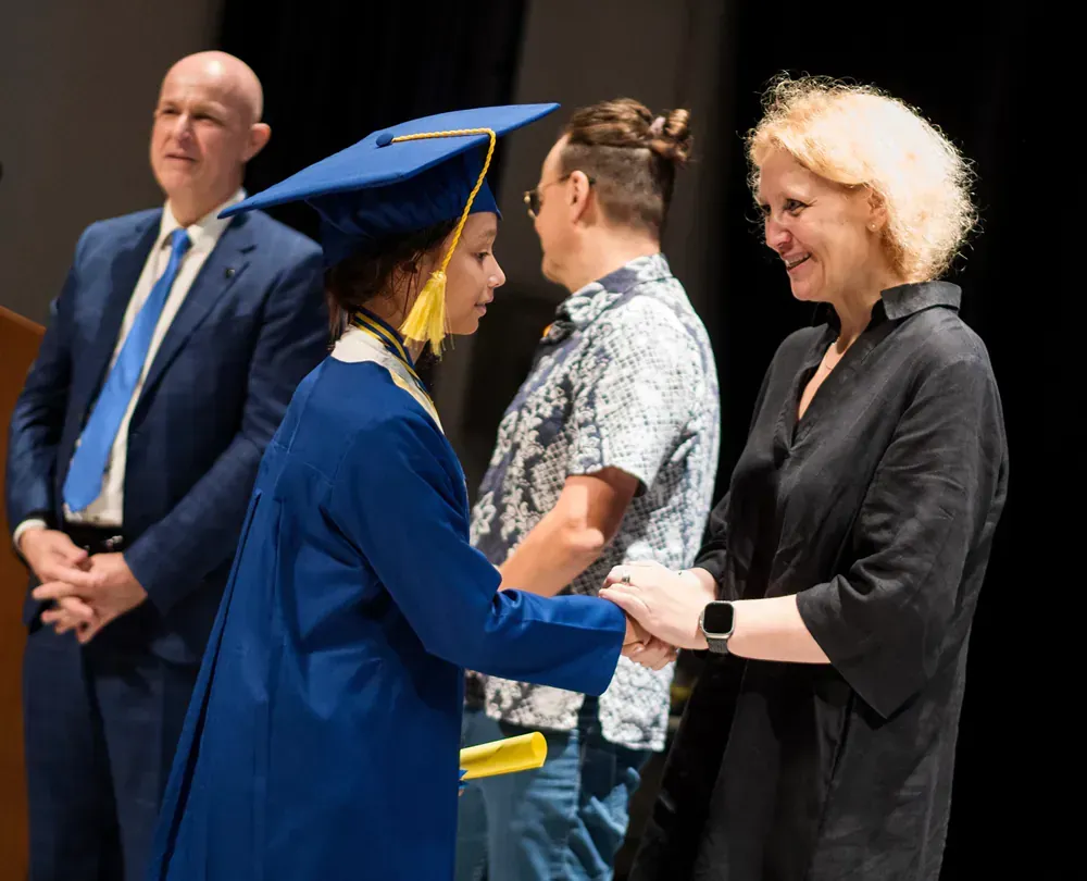 A woman in a blue graduation cap and gown is shaking hands with a man.