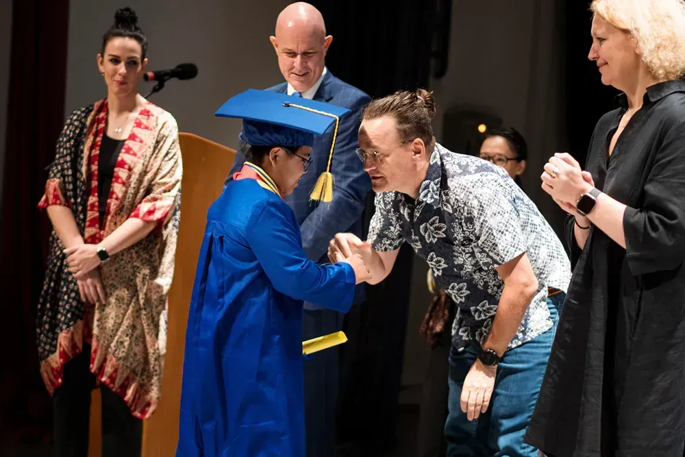A man is shaking hands with a woman in a graduation cap and gown.