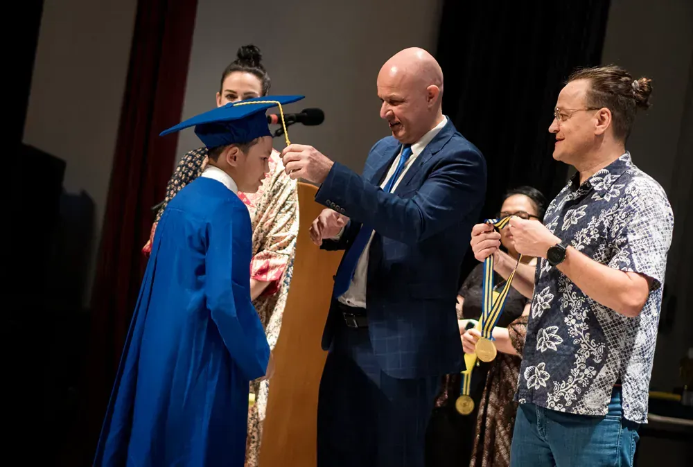 A man in a suit is giving a medal to a boy in a graduation cap and gown.