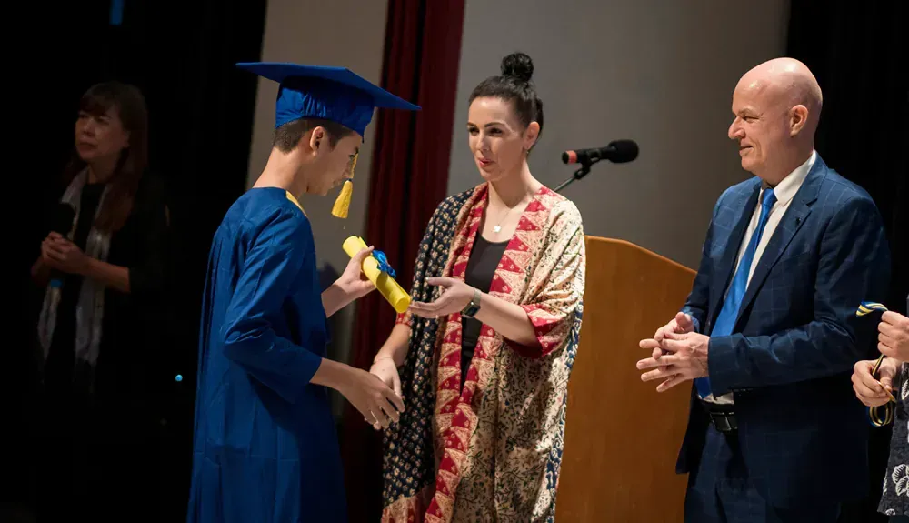 A man in a graduation cap and gown is giving a diploma to a woman.