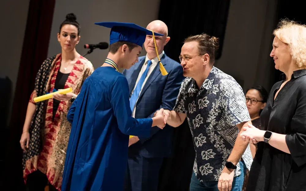 A man is shaking hands with a graduate in a cap and gown.