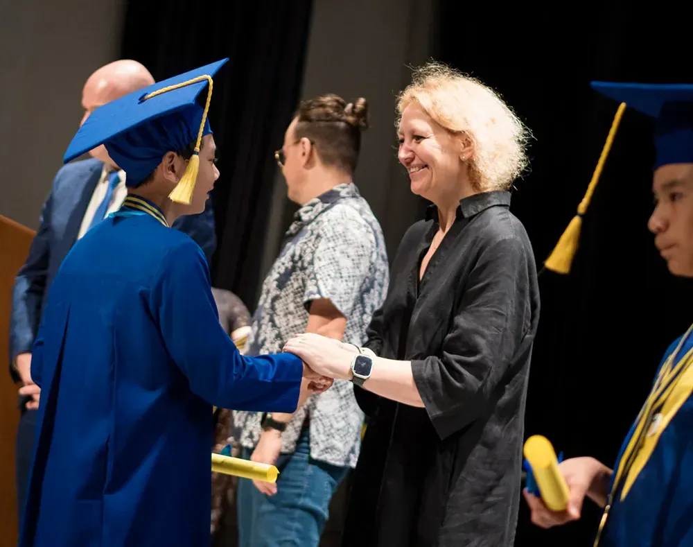 A woman is shaking hands with a graduate at a graduation ceremony.
