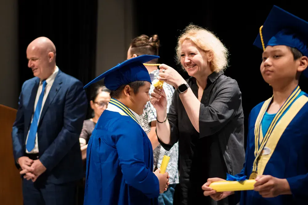 A woman is taking a picture of a boy in a graduation cap and gown.
