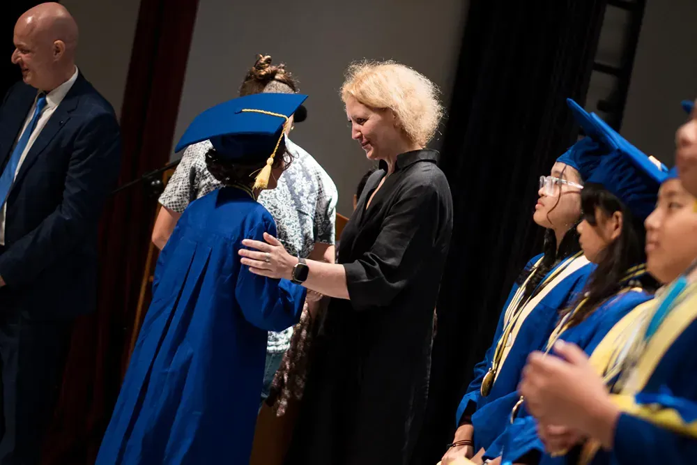 A woman is shaking hands with a graduate in a blue cap and gown.