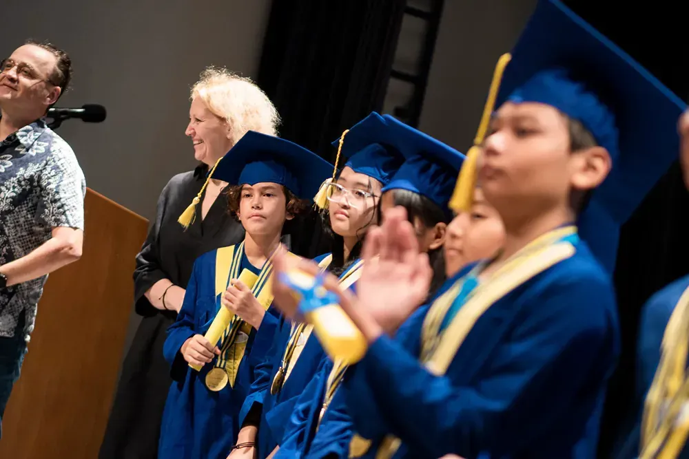 A group of children wearing graduation caps and gowns are standing in front of a podium.