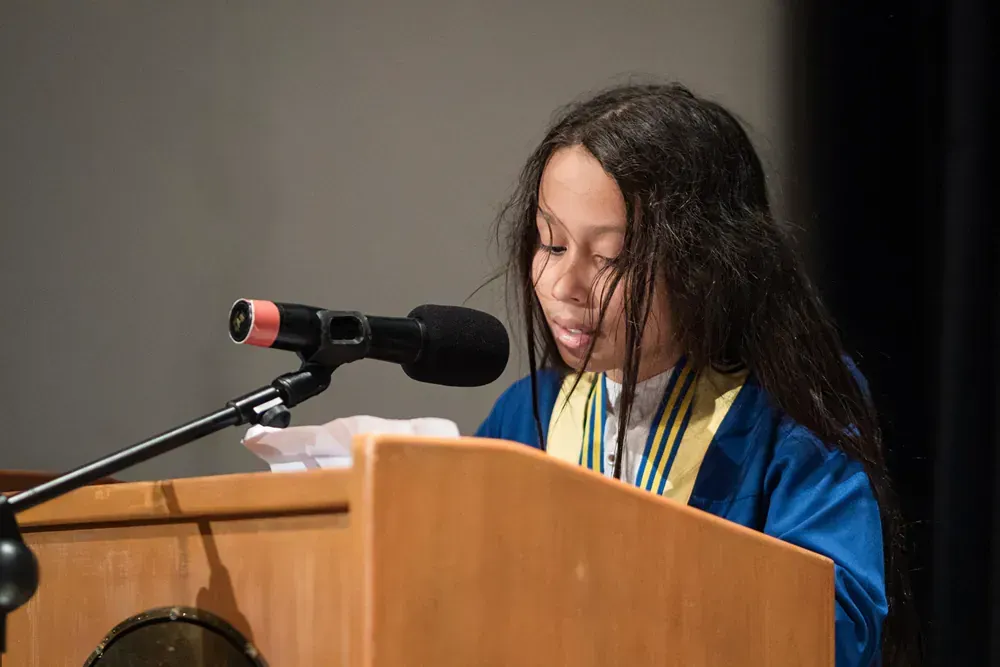 A young girl is giving a speech at a podium in front of a microphone.