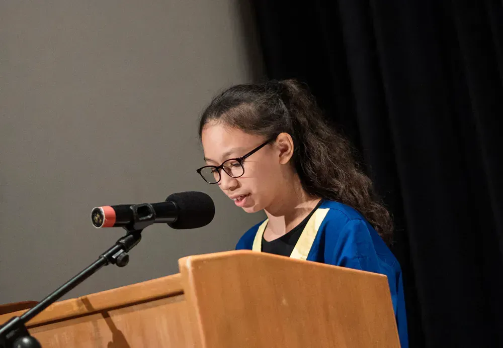 A young girl is standing at a podium speaking into a microphone.