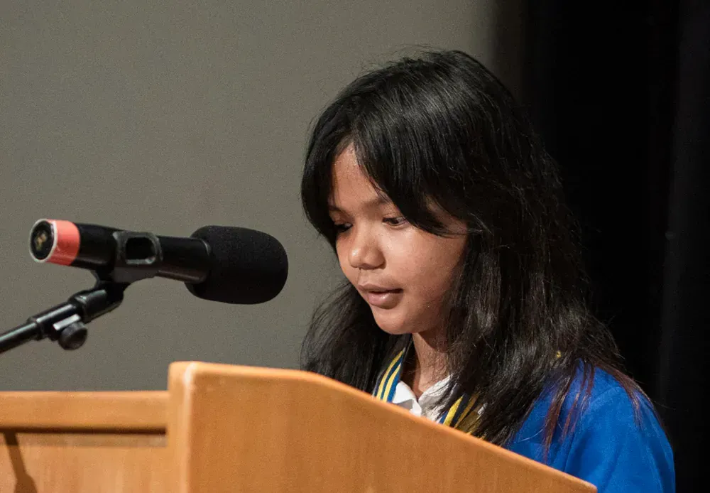 A young girl is standing at a podium speaking into a microphone.