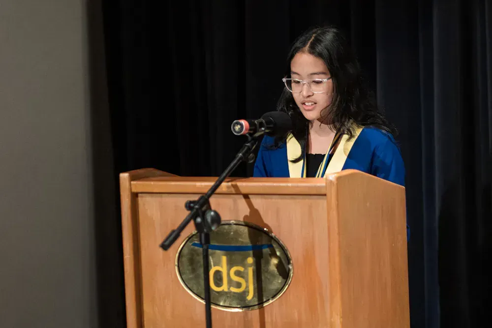 A young woman is standing at a podium speaking into a microphone.