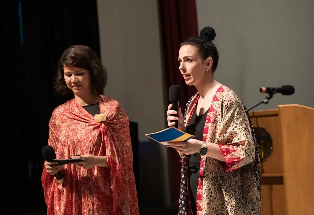 Two women are standing next to each other on a stage holding microphones.