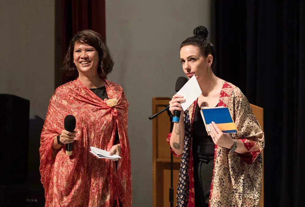 Two women are standing next to each other on a stage holding microphones.