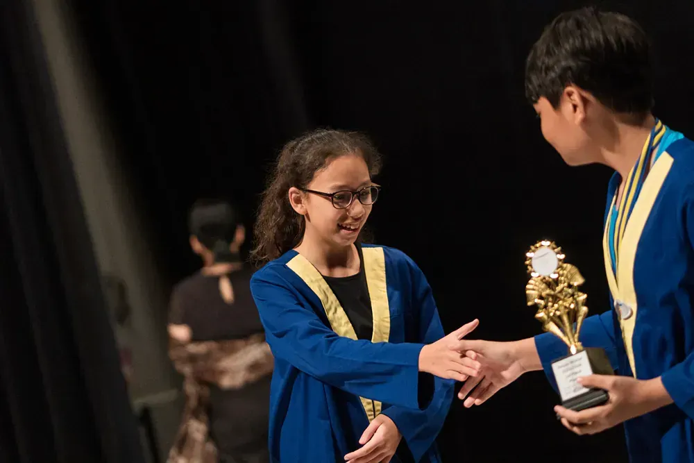 A boy and a girl are shaking hands while holding a trophy.