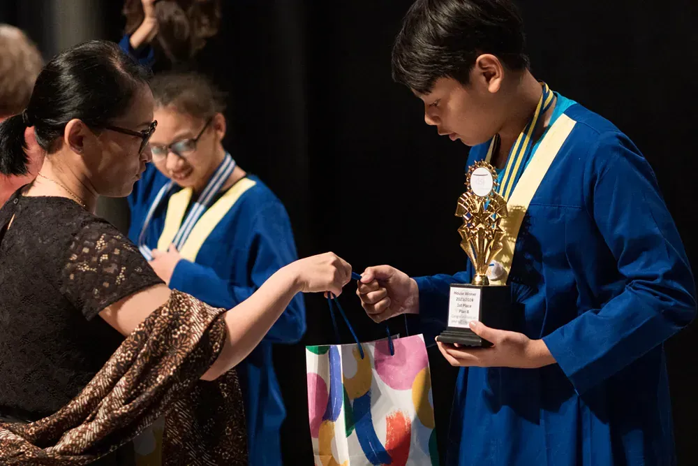 A woman is handing a trophy to a boy who is wearing a medal around his neck.