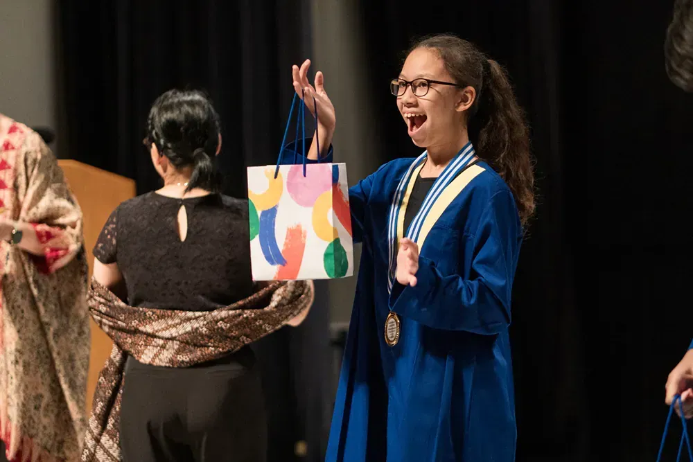 A girl in a graduation cap and gown is holding a gift bag.