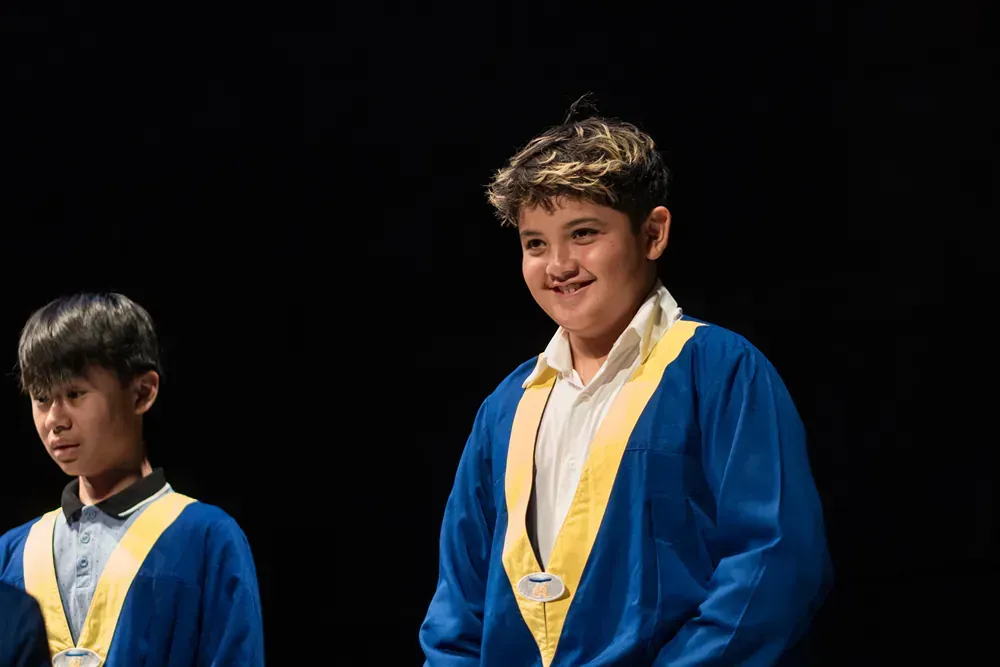 Two young boys in graduation gowns are standing next to each other on a stage.