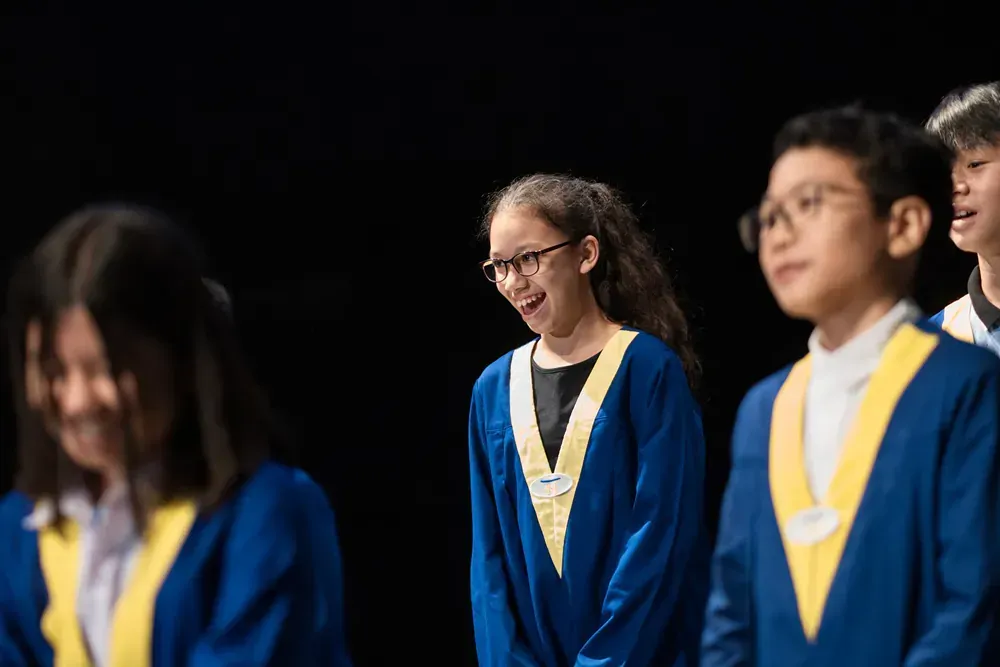A group of children in graduation gowns are standing in a row on a stage.