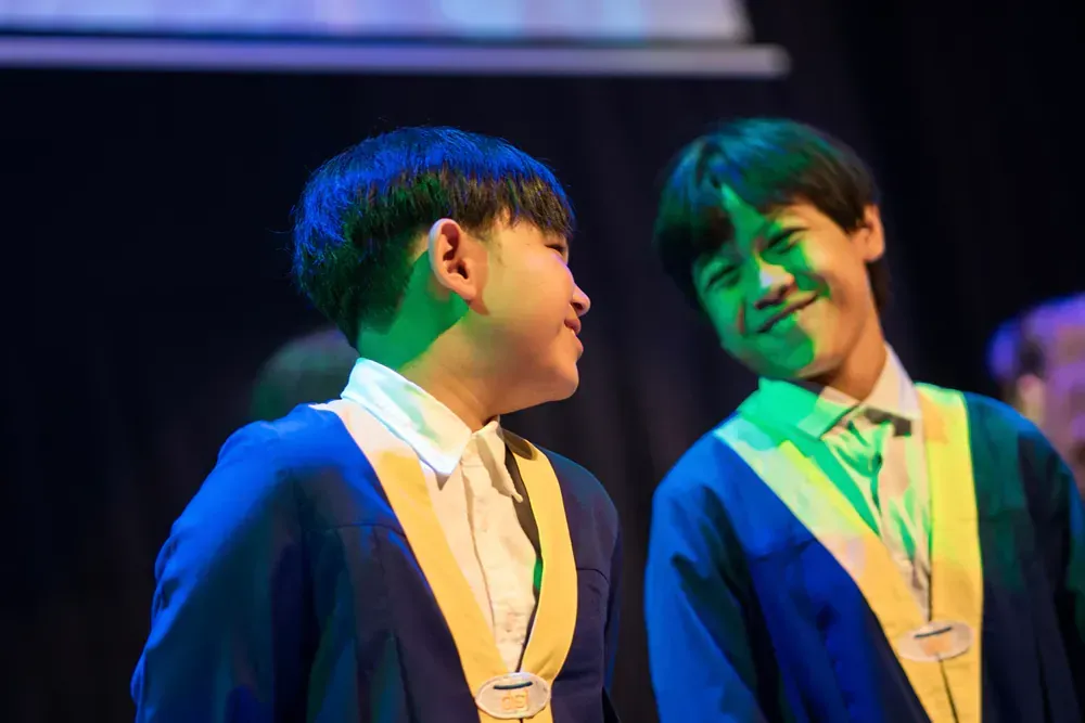 Two young boys in graduation gowns are standing next to each other on a stage.