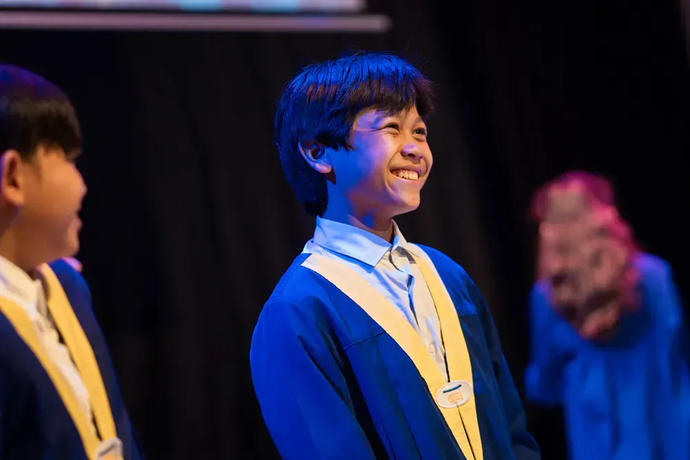 A boy in a graduation cap and gown is smiling on a stage.